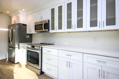 Kitchen with stainless steel appliances, wood finished floors, light countertops, white cabinets, and glass insert cabinets