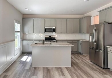 Kitchen with stainless steel appliances, gray cabinets, a sink, light stone counters, and a center island with sink
