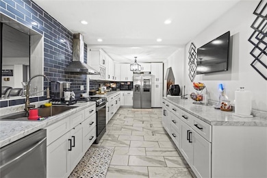 Kitchen featuring appliances with stainless steel finishes, wall chimney exhaust hood, light marble finish flooring, recessed lighting, and white cabinets