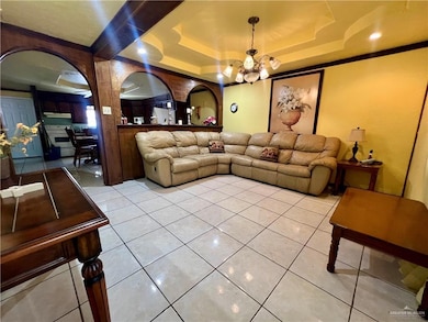 Living area with a tray ceiling, crown molding, a chandelier, and tile patterned floors