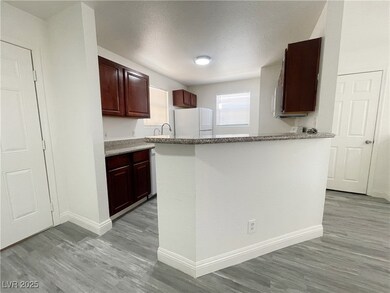 Kitchen with freestanding refrigerator, light wood-style floors, light stone counters, and a textured ceiling