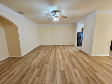 Unfurnished room with a ceiling fan, light wood-style floors, arched walkways, and ornamental molding