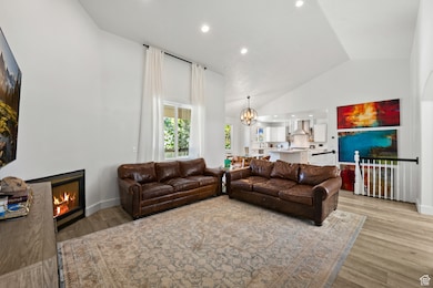 Living room with a chandelier, recessed lighting, a glass covered fireplace, light wood finished floors, and high vaulted ceiling
