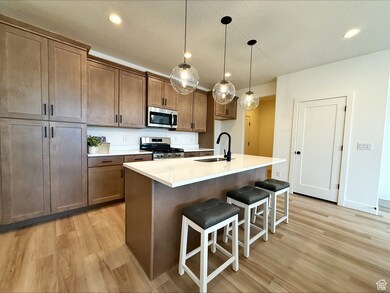 Kitchen featuring decorative light fixtures, stainless steel appliances, a breakfast bar area, a center island with sink, and light wood-style floors