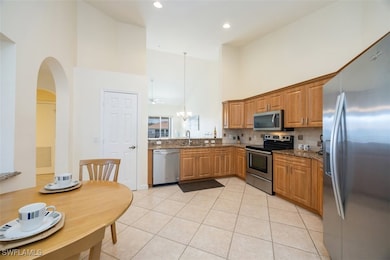 Kitchen with appliances with stainless steel finishes, a towering ceiling, light tile patterned flooring, decorative backsplash, and hanging light fixtures
