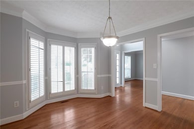 Unfurnished dining area featuring wood finished floors, baseboards, a textured ceiling, and crown molding