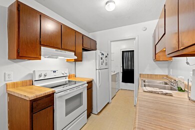 Kitchen featuring white range with electric stovetop, under cabinet range hood, light countertops, light floors, and separate washer and dryer