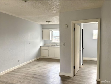 Kitchen with a textured wall, a textured ceiling, light wood-style floors, light countertops, and white cabinetry