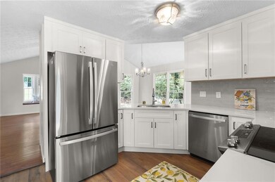 Kitchen with lofted ceiling, appliances with stainless steel finishes, a textured ceiling, light countertops, and white cabinetry