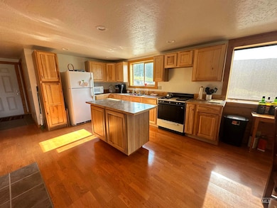 Kitchen with white appliances, a textured ceiling, wood finished floors, a center island, and light countertops