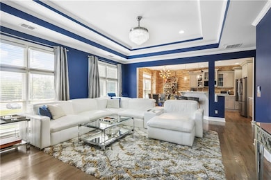Living room with a chandelier, a tray ceiling, ornamental molding, and dark wood finished floors