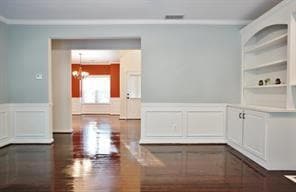 Spare room with a decorative wall, a wainscoted wall, a chandelier, ornamental molding, and dark wood finished floors