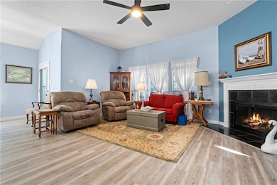 Living room with a tile fireplace, wood finished floors, a ceiling fan, a textured ceiling, and lofted ceiling