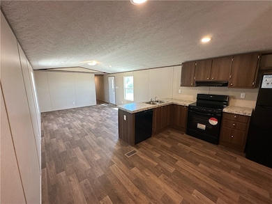 Kitchen featuring a peninsula, light countertops, black appliances, open floor plan, and a textured ceiling