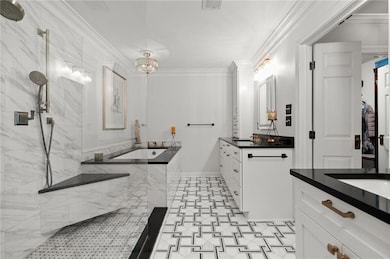 Full bathroom with two vanities, crown molding, a bath, a marble finish shower, and baseboards