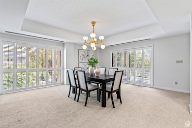 Dining area with a raised ceiling, light carpet, and a chandelier