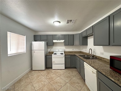 Kitchen with gray cabinetry, white appliances, a textured ceiling, light tile patterned flooring, and under cabinet range hood