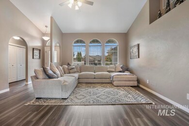 Living room with dark wood-style floors, arched walkways, a ceiling fan, and high vaulted ceiling