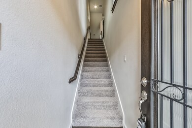 A welcoming entryway with a carpeted staircase leading to the upper level, featuring a stylish metal door and neutral wall tones for a modern touch.