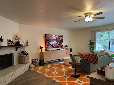 Living area featuring wood finished floors, a brick fireplace, ceiling fan, and a textured ceiling