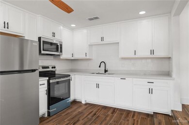 Kitchen with sink, white cabinets, backsplash, stainless steel appliances, and dark wood-type flooring