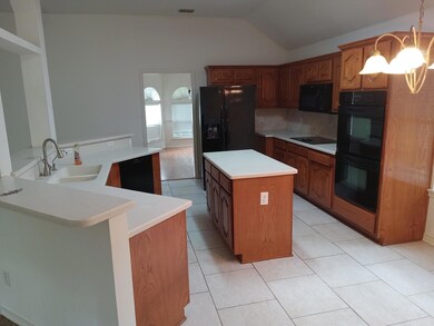 Kitchen with vaulted ceiling, black appliances, backsplash, a center island, and sink