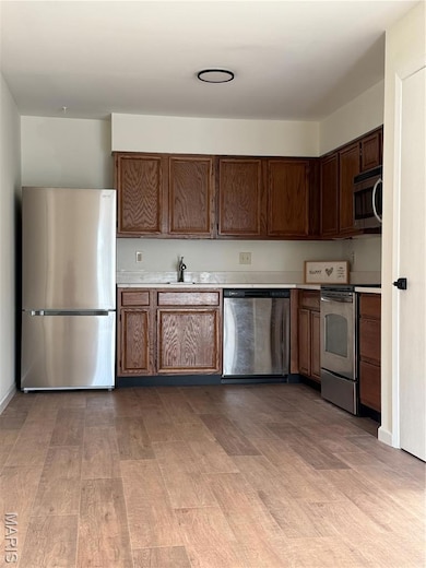 Kitchen featuring fridge, light countertops, dishwasher, range, and light wood finished floors