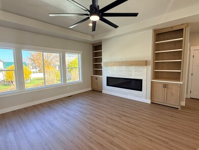 Unfurnished living room featuring a glass covered fireplace, a ceiling fan, light wood finished floors, and built in features