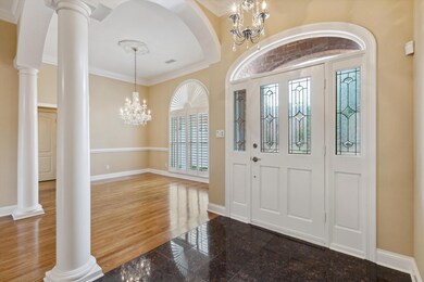Entrance foyer featuring a chandelier, granite tiled floors, baseboards, crown molding, and decorative columns