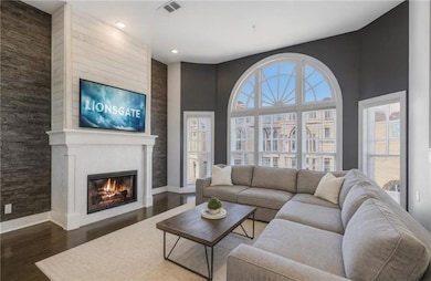 Living room with a fireplace, dark wood-style flooring, recessed lighting, an accent wall, and a towering ceiling