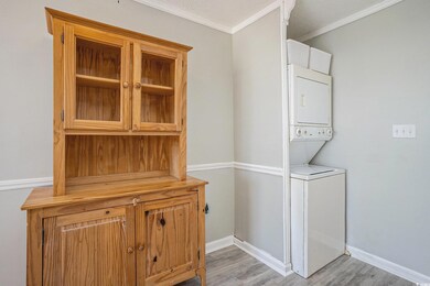 Laundry view of estacked washer and dryer, crown molding, and wood finished floors