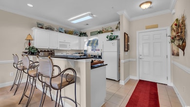 Kitchen with white appliances, a breakfast bar area, dark countertops, a peninsula, and white cabinetry