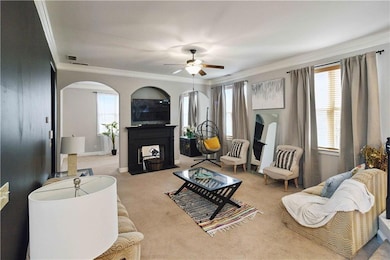 Living room featuring arched walkways, a ceiling fan, crown molding, carpet, and healthy amount of natural light