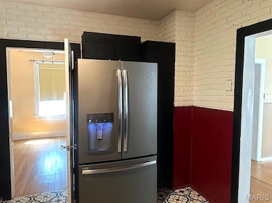 Kitchen featuring stainless steel refrigerator with ice dispenser, brick wall, and light wood-style floors
