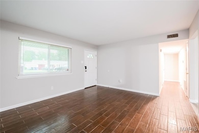 Unfurnished living room featuring dark wood-style floors and baseboards
