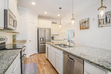 Kitchen featuring stainless steel appliances, light wood-style flooring, ornamental molding, white cabinetry, and decorative backsplash