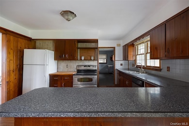 Kitchen with freestanding refrigerator, stainless steel electric range, backsplash, and brown cabinets