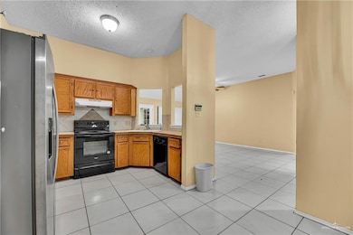 Kitchen with black appliances, brown cabinetry, decorative backsplash, light tile patterned floors, and a textured ceiling