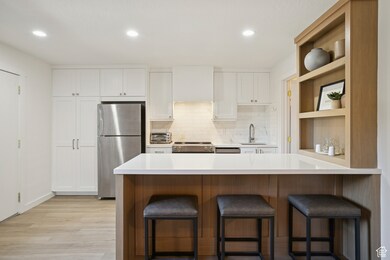 Kitchen with a kitchen bar, white cabinetry, decorative backsplash, stainless steel appliances, and a peninsula