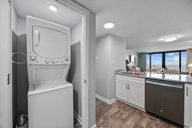 Washroom with dark wood-style floors and stacked washer / dryer