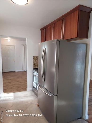 Kitchen featuring freestanding refrigerator, light tile patterned floors, brown cabinets, and range