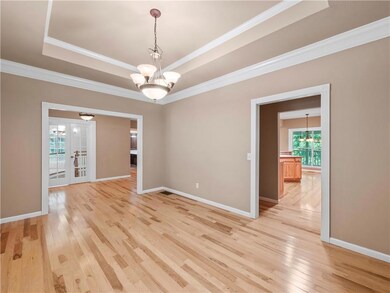 Spare room with a chandelier, light wood-style flooring, crown molding, a tray ceiling, and french doors