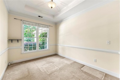 Carpeted spare room featuring baseboards, ornamental molding, and a raised ceiling