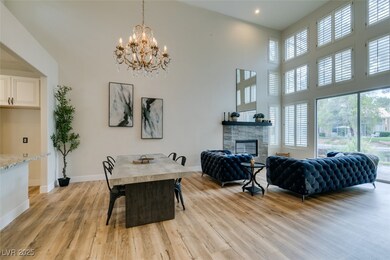 Dining space with light wood-style floors, a stone fireplace, a chandelier, a towering ceiling, and recessed lighting