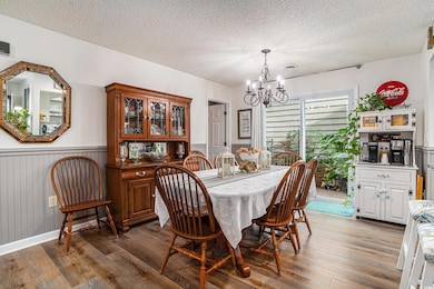 Dining room with a chandelier, a textured ceiling, wood finished floors, and wainscoting