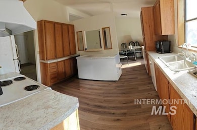 Kitchen featuring brown cabinets, dark wood-type flooring, light countertops, white appliances, and ventilation hood