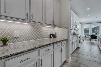 Convenient butler's pantry is located between the formal dining room and kitchen and offers granite countertop with fabulous upgraded tile backsplash and plenty of cabinetry accented by brushed nickel hardware. Perfect space for serving buffet-style, bar set-up, and for storing serving pieces. On the opposite wall, you'll find the door to the oversized pantry.