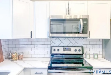 Kitchen featuring stainless steel appliances, white cabinets, decorative backsplash, and light stone countertops