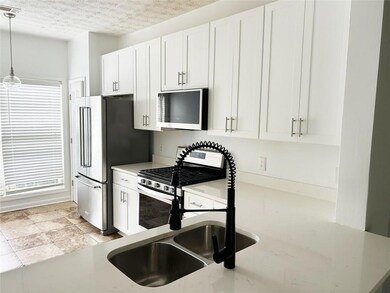Kitchen featuring stainless steel appliances, pendant lighting, white cabinetry, a textured ceiling, and light stone countertops