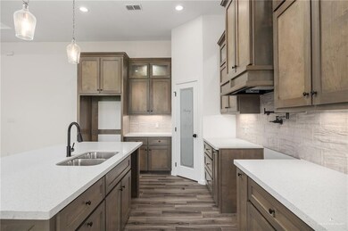 Kitchen with pendant lighting, dark hardwood / wood-style flooring, backsplash, sink, and an island with sink